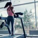 Young woman running on a treadmill while looking out of a window.