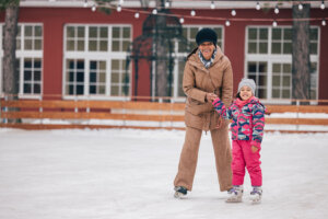 A woman and young girl hold hands while ice skating on an outdoor rink.