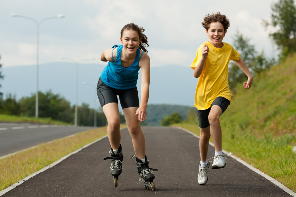 A girl Rollerblades on a paved path next to a boy who is running. 