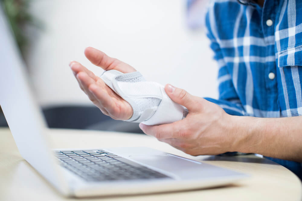 A man holds a splinted wrist and hand while sitting in front of a computer. 