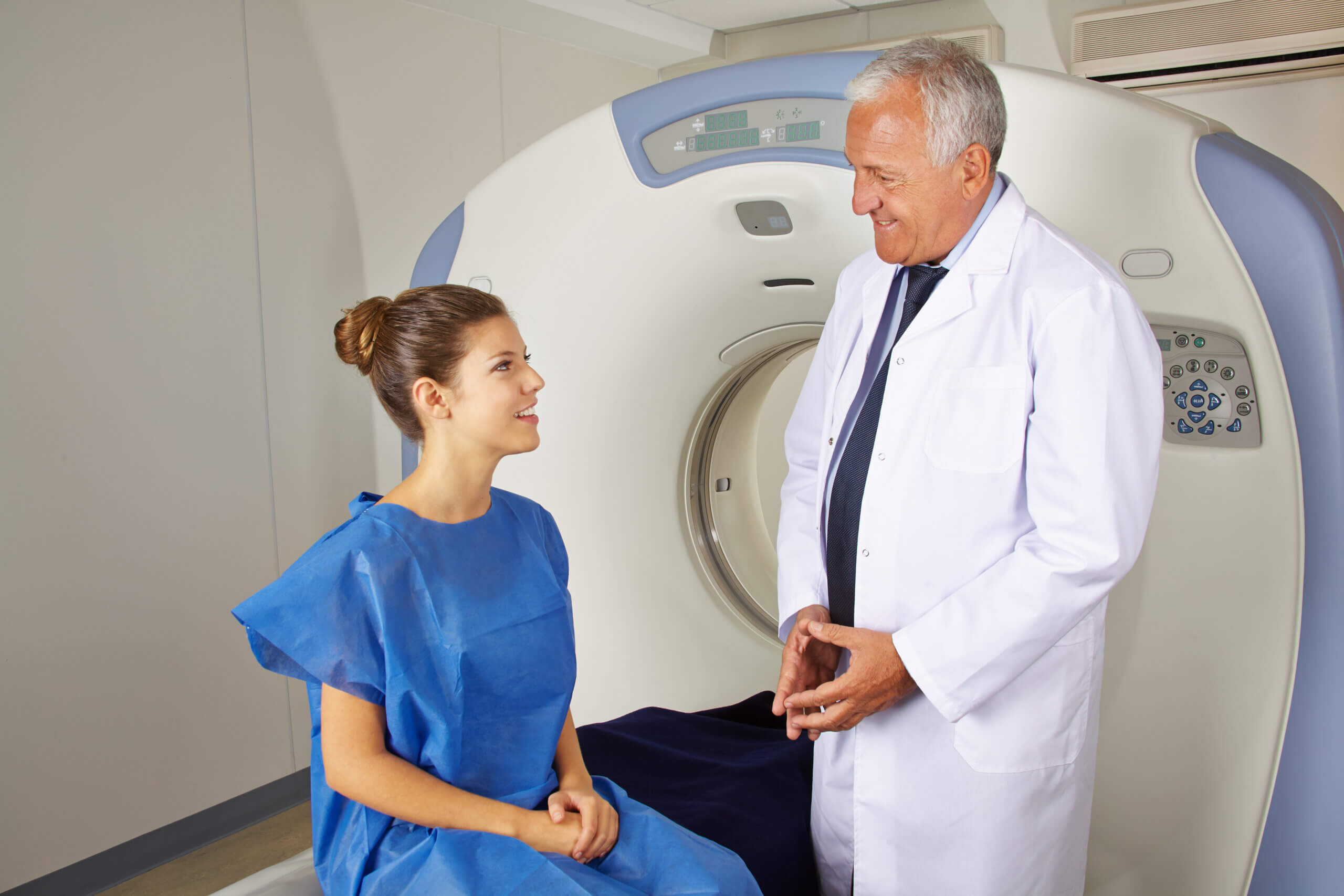 A doctor prepping his patient as she sits on the MRI machine bed.