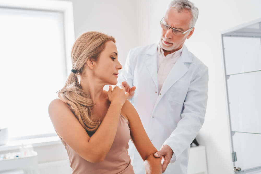  An older male doctor examines a younger female patient’s shoulder. 