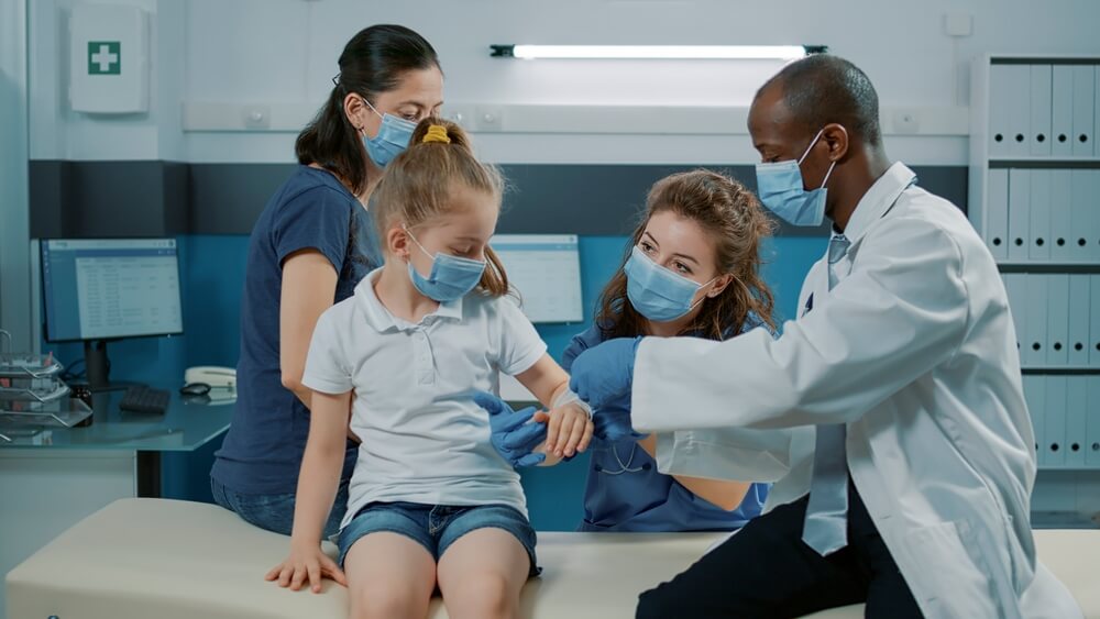 A male doctor examines a young girl’s arm while two nurses look on behind her. 