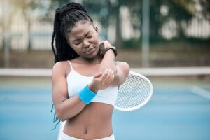 A young woman with a racquet on a tennis court holds her elbow in pain.