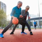 An older man and woman play basketball on an outdoor court.