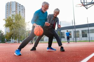 An older man and woman play basketball on an outdoor court.