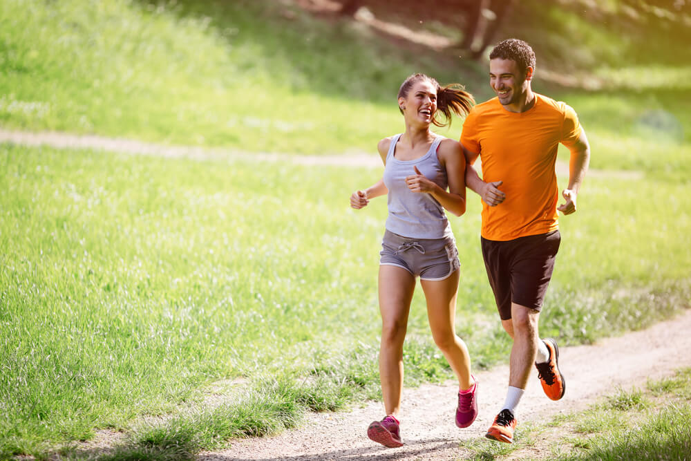A young couple runs outside on a trail. 