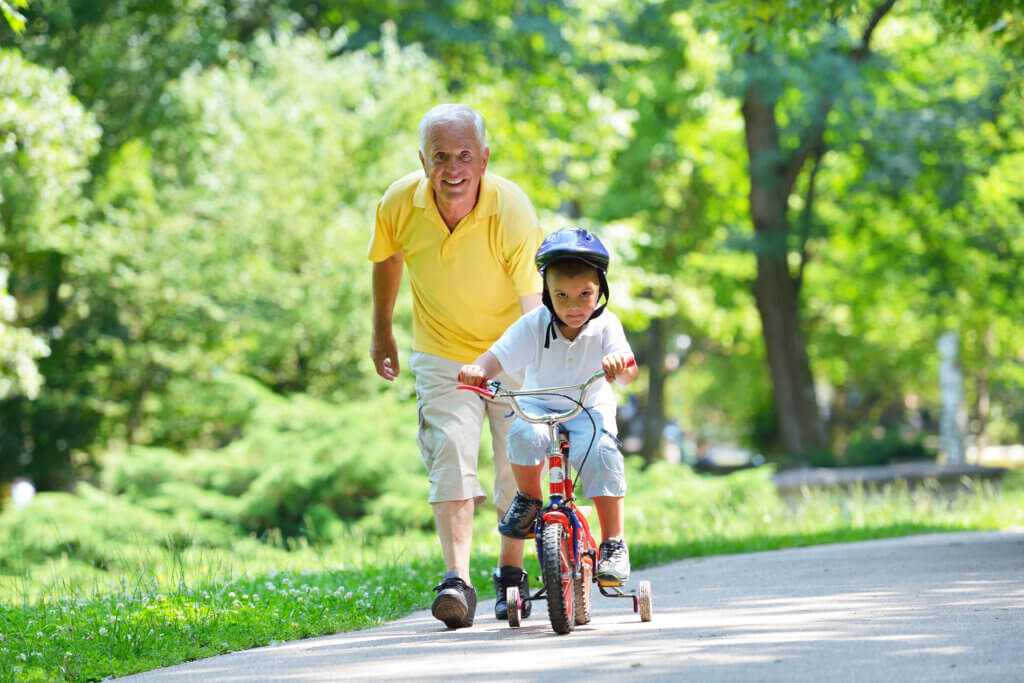 Happy grandfather playing in the park with his grandson. Grandson is on his bike and grandfather is running behind him. This grandfather has had a total knee replacement surgery. 