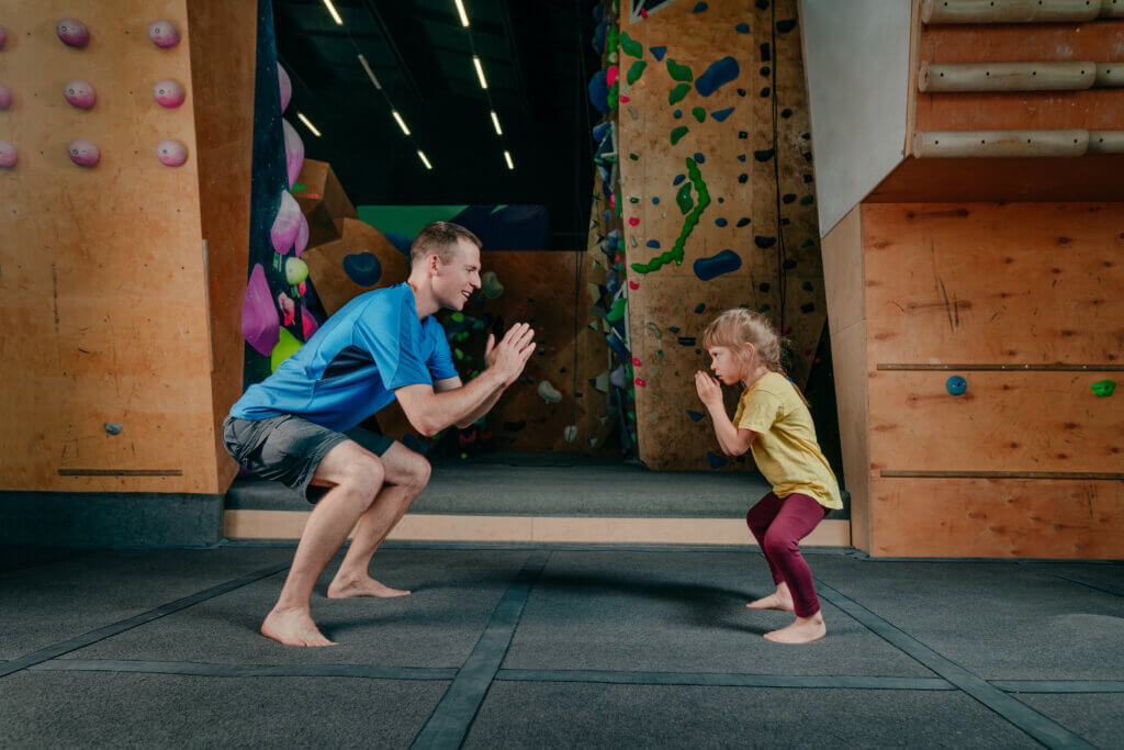 Father and daughter doing squats in a gym. Father has recovered from quadriceps tendon injury.