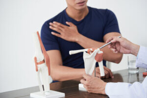 Orthopedic doctor discussing shoulder joint pain with a patient using a shoulder model