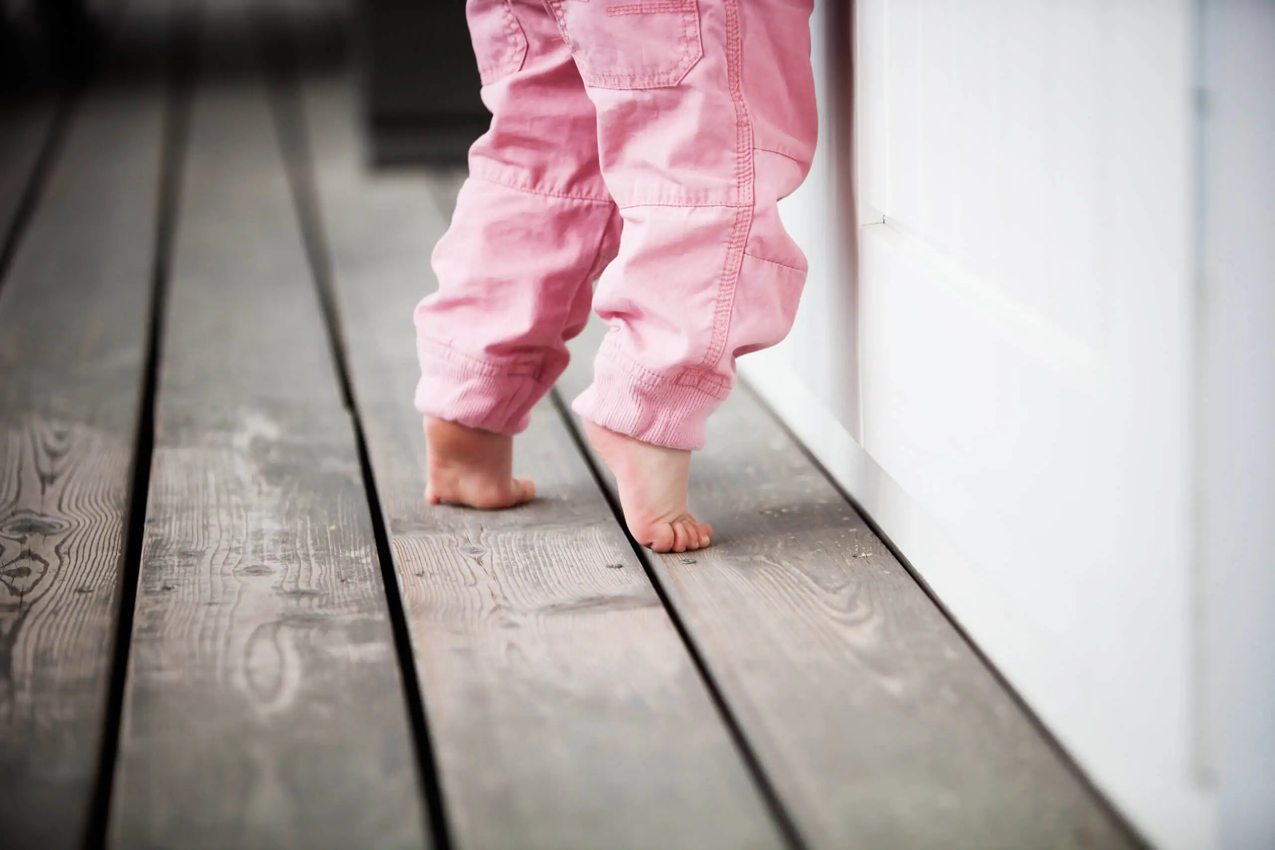 A little girl in pink pants stands on her toes. 