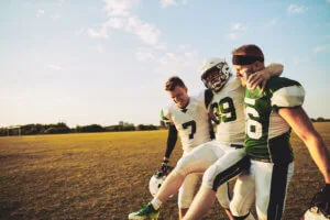 Two young football players help their injured teammate off the field. 