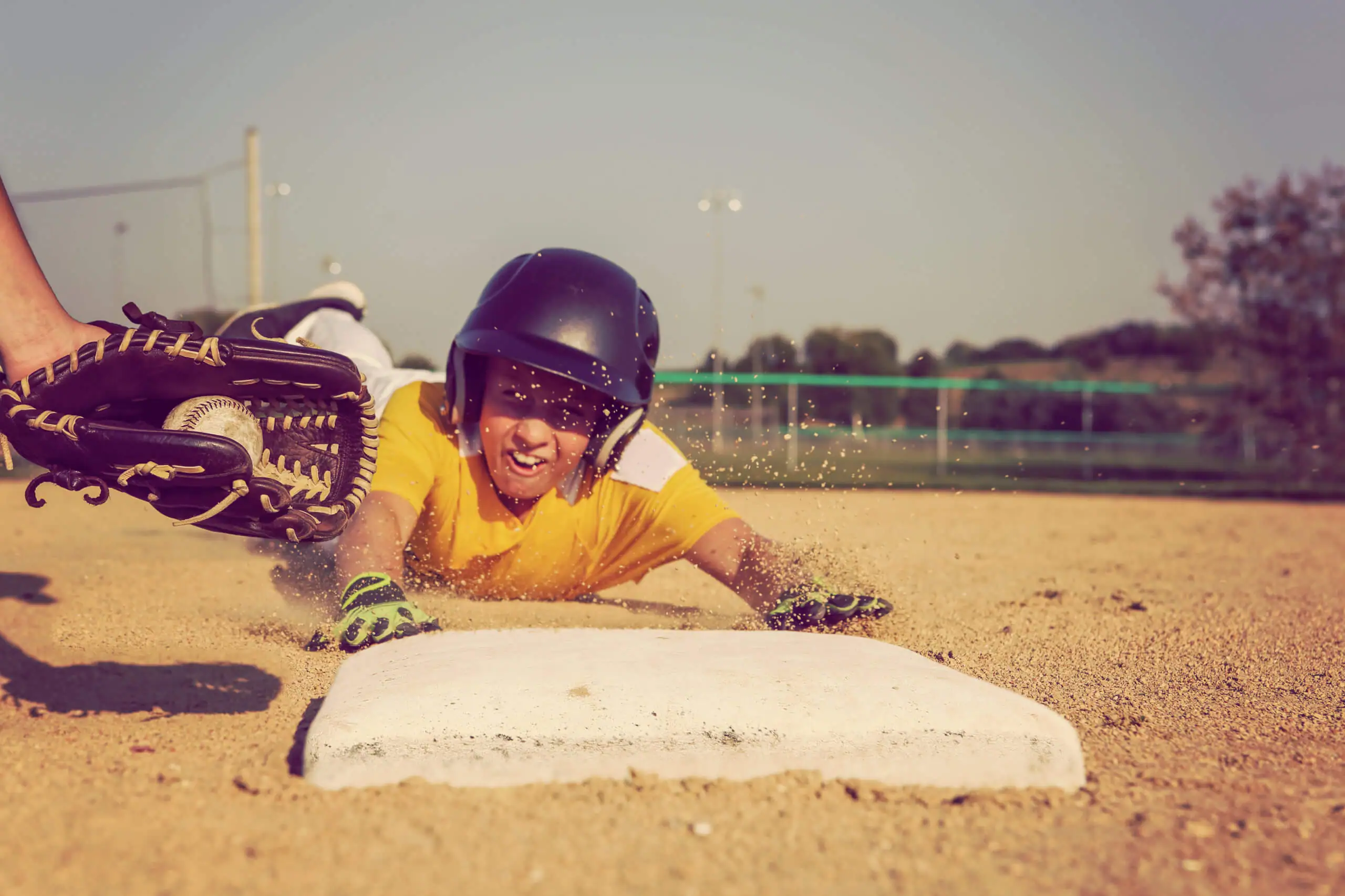 A boy slides into a base while another player reaches out to him with a ball and glove.